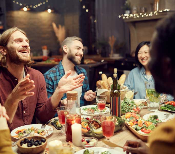 Group of young adults laughing and enjoying dinner at a restaurant.